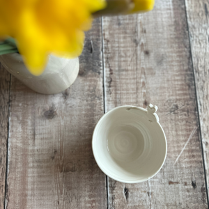 Handmade Porcelain Bowl with Easter Bunny Sat atop it on a wooden table next to a vase of daffodils