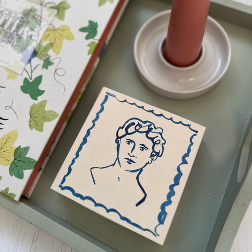 The Handsome Luxury Square Matches on a tray with a book on interiors and a handmade candle holder with a pink stubby candle